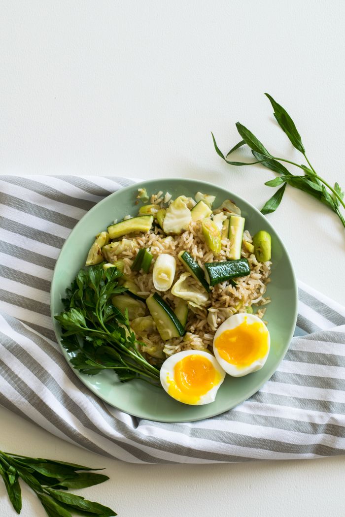 Contact A top view of a healthy vegetable rice dish with soft-boiled eggs on a light green plate.